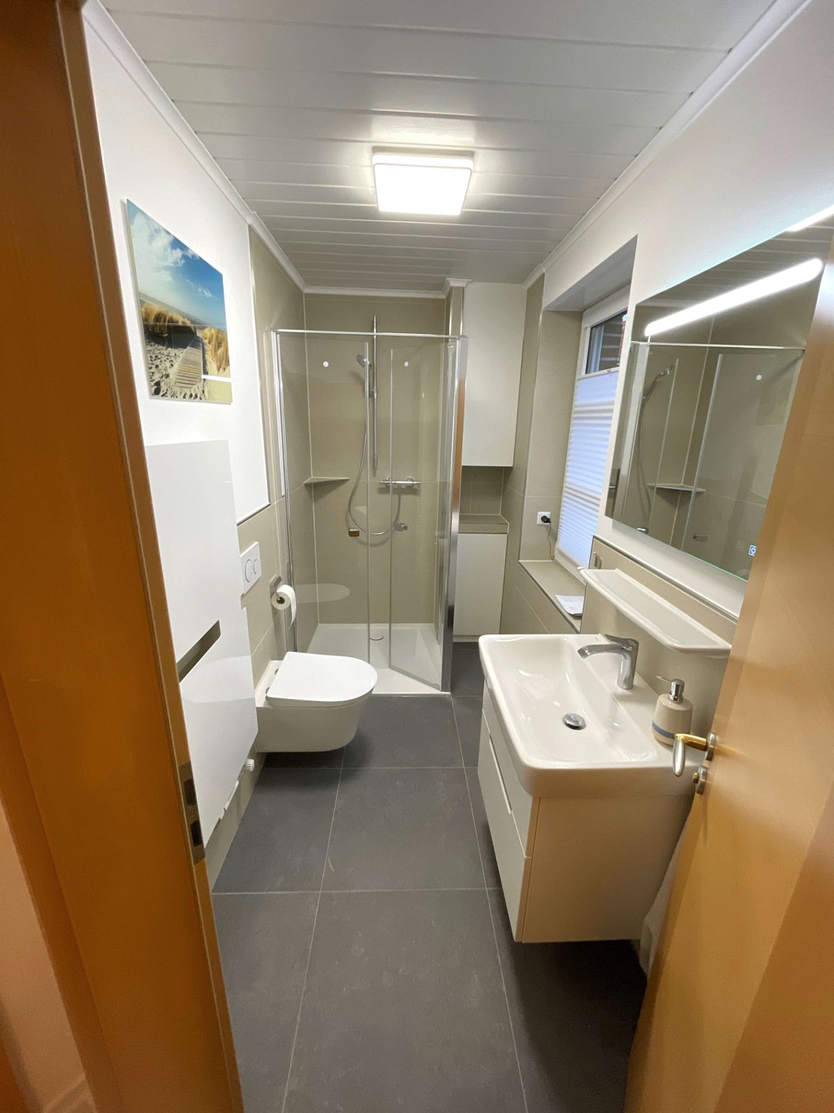 Schmales Bad nach der Sanierung: Eck-Duschkabine, Wand-WC und Waschtisch mit Unterschrank in einem langen Grundriss