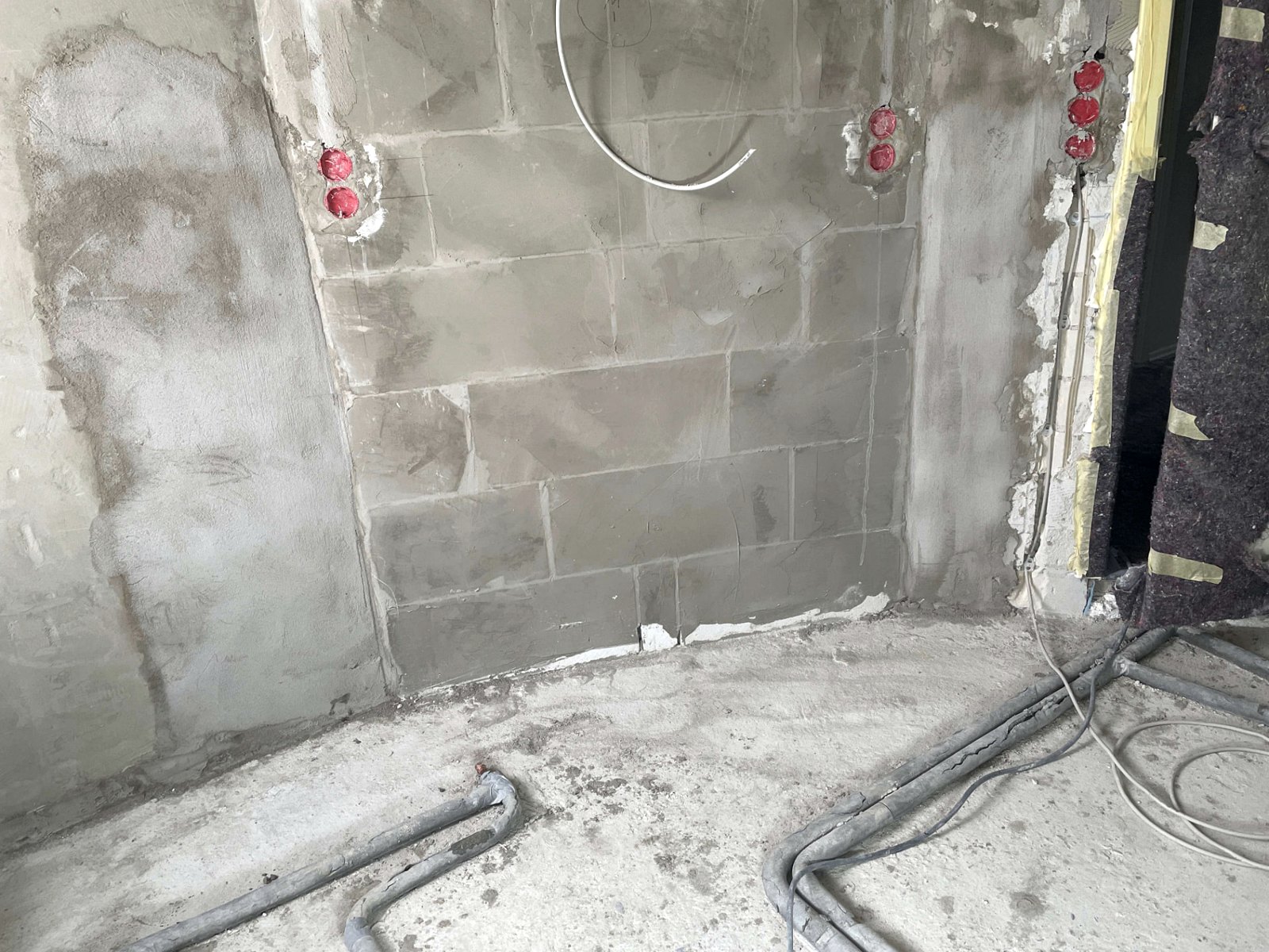 Bauphase: verputzte Rohbauwand mit gesetzten Elektrodosen und Leerrohren für Waschplatz und Duschbereich