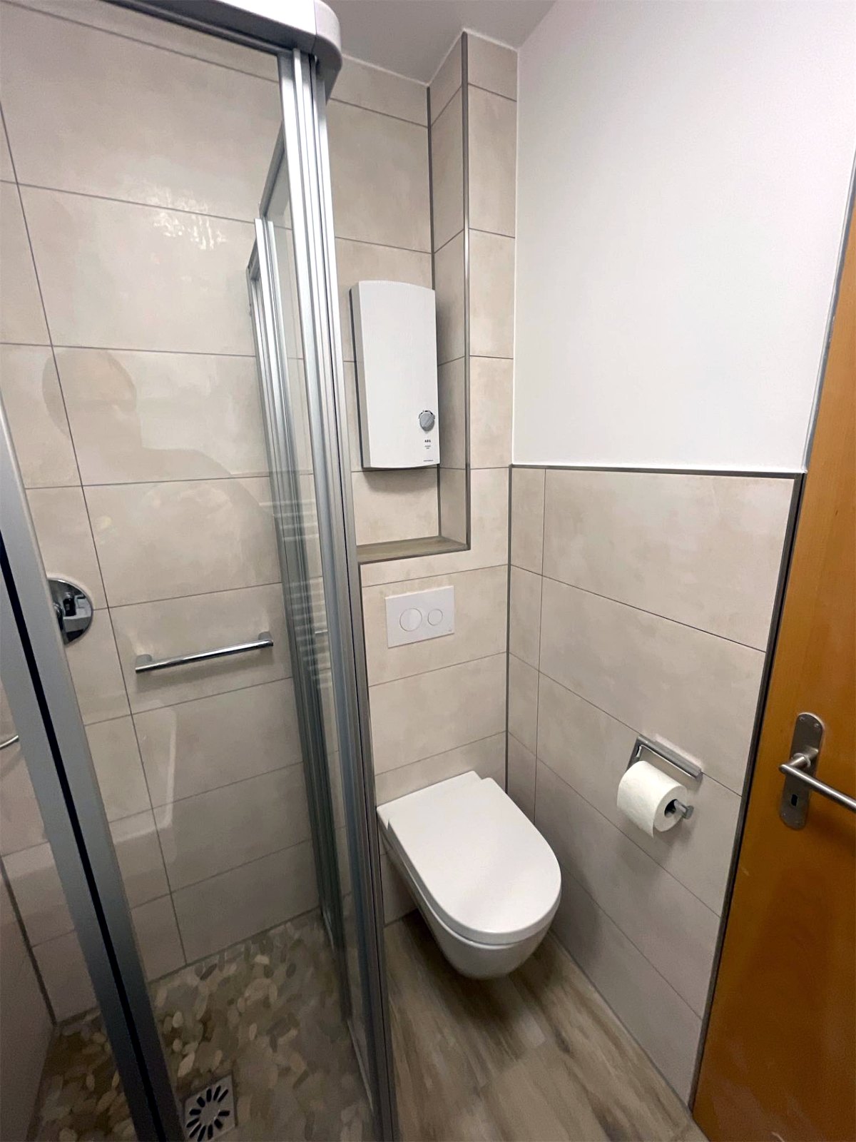 Wand-WC mit Unterputz-Spülkasten neben der Duschkabine, Durchlauferhitzer in einer gefliesten Nische