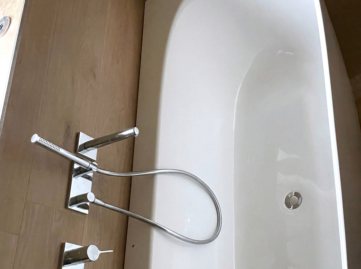 Freistehende Badewanne mit Wandarmatur und Handbrause vor Fliesen in Holzoptik