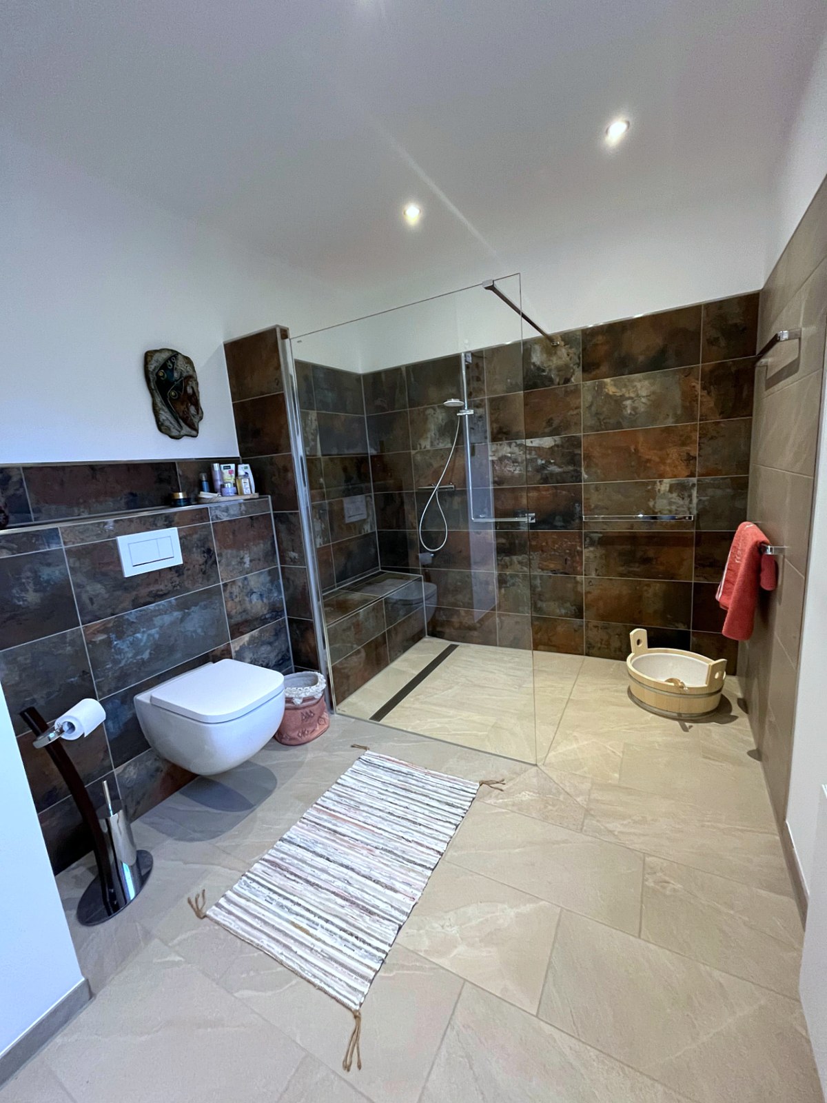 Saniertes Bad mit bodengleicher Walk-in-Dusche, Glastrennwand, gemauerter Sitzbank, Wand-WC und großformatigen Fliesen in Metalloptik