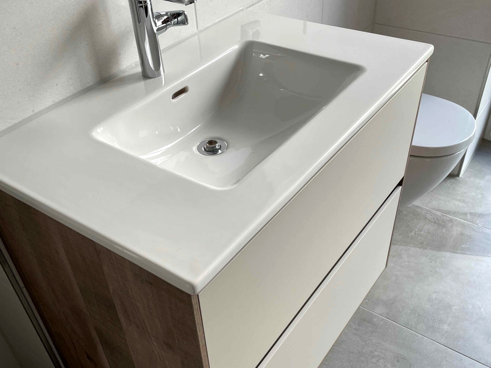 Waschtisch mit Keramikplatte und Holzfront, im Hintergrund Wand-WC in einem hellen Bad
