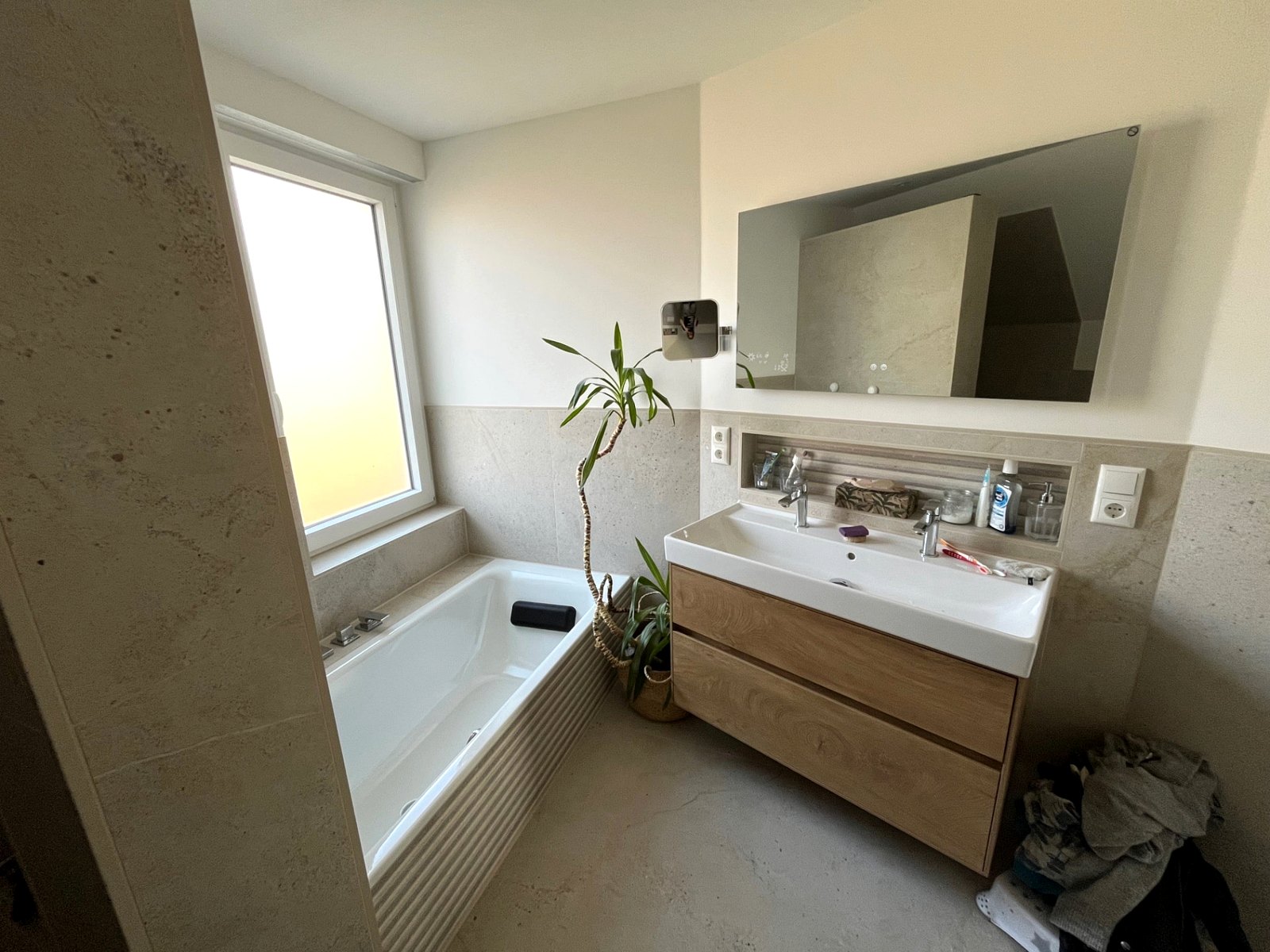 Fertiges Bad mit Badewanne am Fenster, Doppelwaschtisch auf Holzunterschrank, Spiegelheizung und Ablagenische