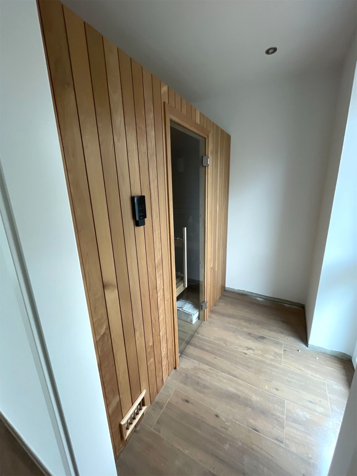 Fertig eingebaute Sauna mit Holzverkleidung, Glastür, Steuerung an der Front und Lüftungsgitter im Sockel