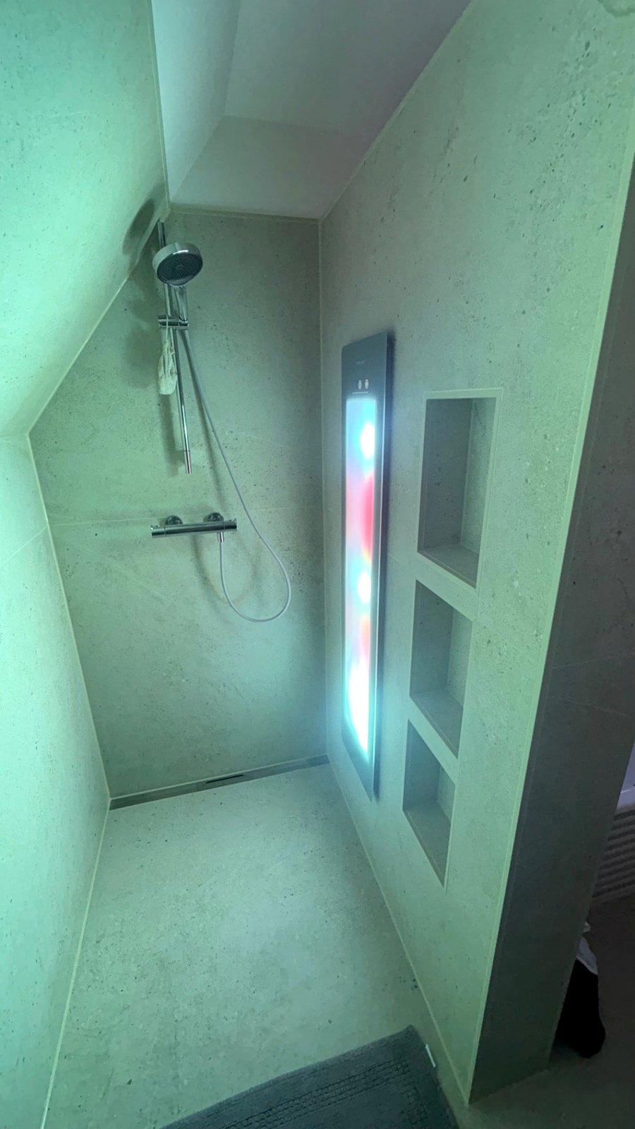 Sunshower-Paneel mit farbigem Licht in einer bodengleichen Dusche unter der Dachschräge, daneben gefliese Ablagenischen