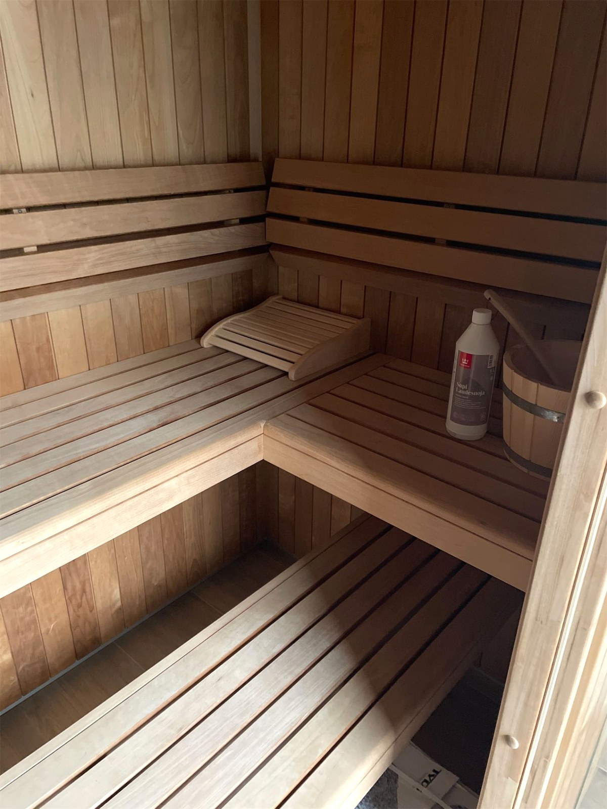 Innenansicht der Sauna mit zwei Bankebenen über Eck, Rückenlehnen, Kopfstütze und Aufgusskübel