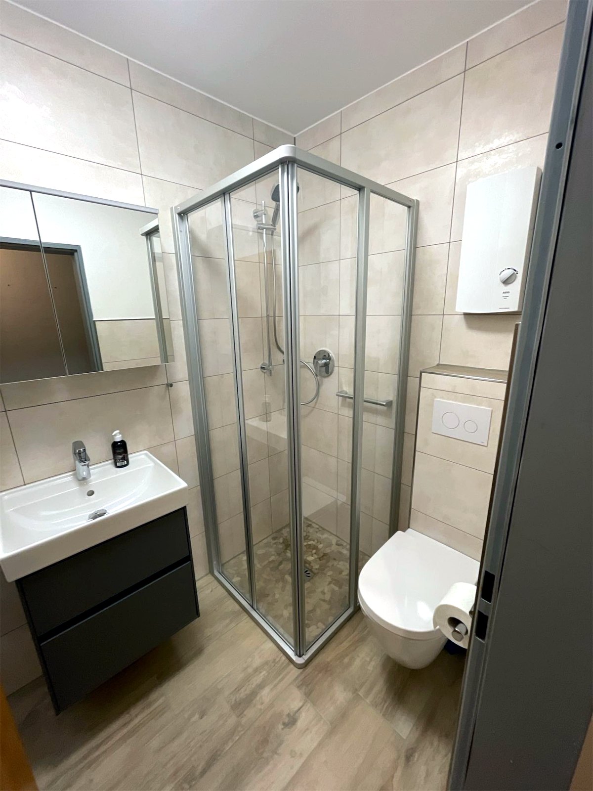 Kleines Bad nach der Sanierung: Waschtisch mit Unterschrank und Spiegelschrank, Eck-Duschkabine und Wand-WC auf wenigen Quadratmetern