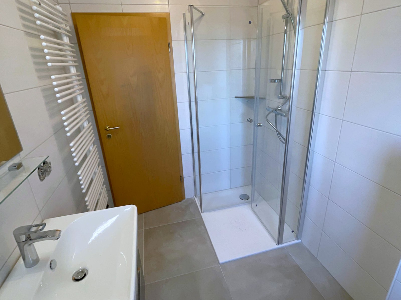 Saniertes Ferienwohnungsbad mit Eck-Duschkabine, flacher Duschwanne, Waschtisch und Handtuchheizkörper