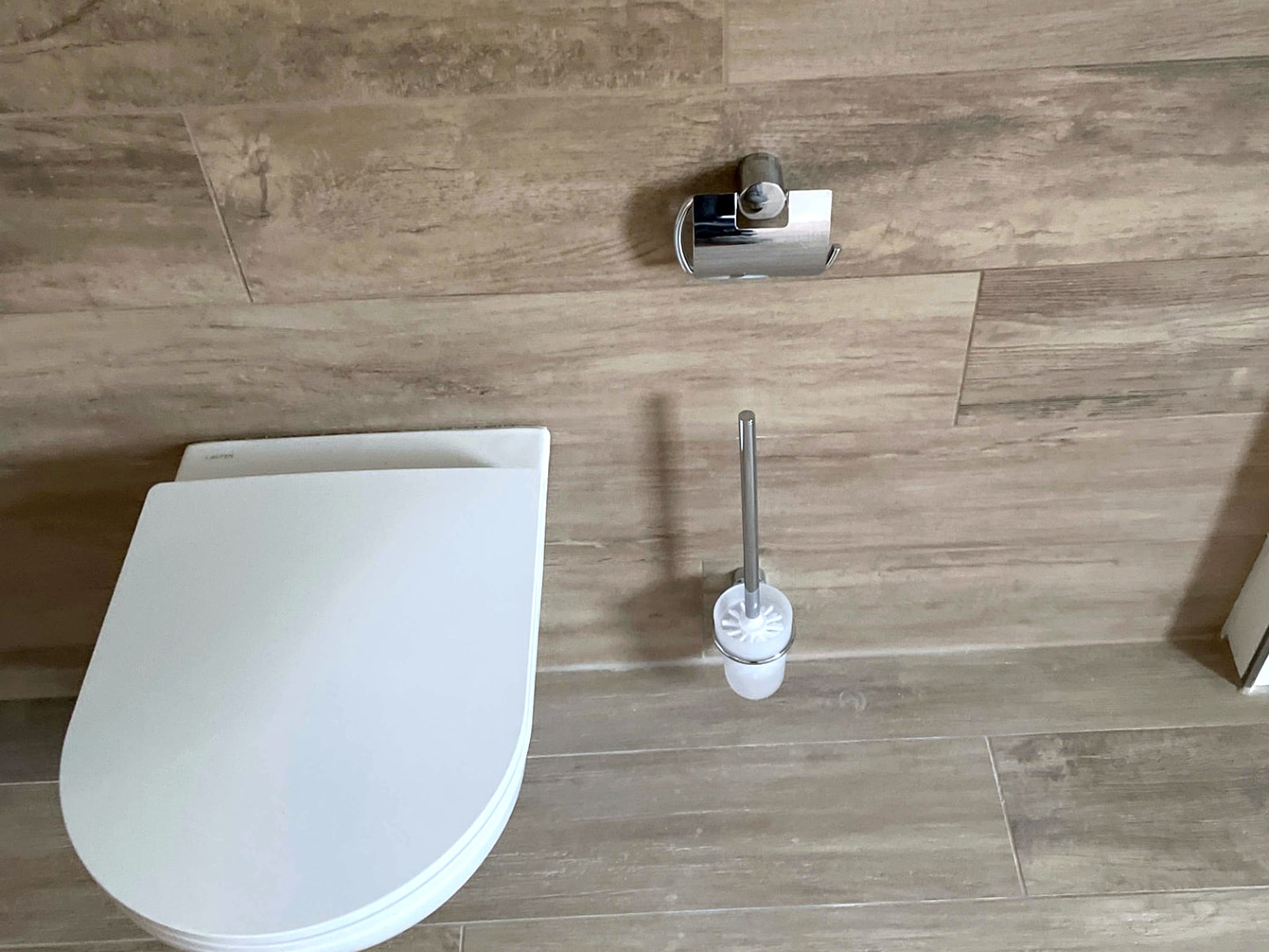 Wand-WC vor Wandfliesen in Holzoptik mit Papierhalter und Bürstengarnitur